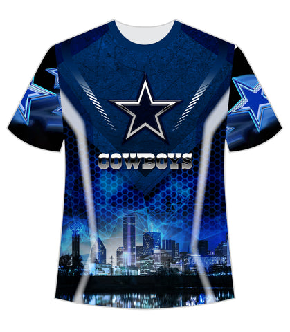 A striking blue t-shirt featuring the Dallas Cowboys logo with a prominent star and the team name "COWBOYS" in bold. The design includes a futuristic cityscape of Dallas with iconic buildings and a reflection on water, accented with hexagonal patterns and glowing blue star elements, perfect for NFL fans.