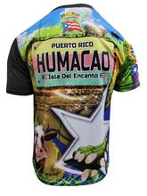 A vibrant t-shirt celebrating Humacao, Puerto Rico as "La Perla del Oriente" with front and back designs. The front features bold text "La Perla del Oriente" with a colorful flag collage, a coat of arms, and a blue gradient background with the Puerto Rican flag. The back showcases a rural landscape with cows, a "Humacao Isla del Encanto" sign, and a large star with a Gufeao logo, perfect for expressing Humacao pride and Puerto Rican heritage.