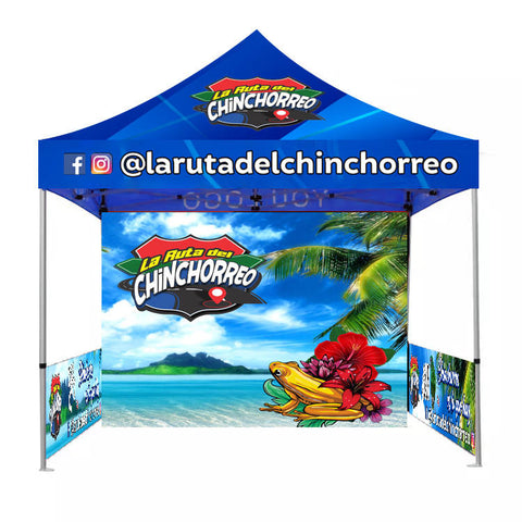 Blue canopy tent with 'La Ruta del Chinchorreo' logo, tropical beach scene, frog, flowers, and social media handles.