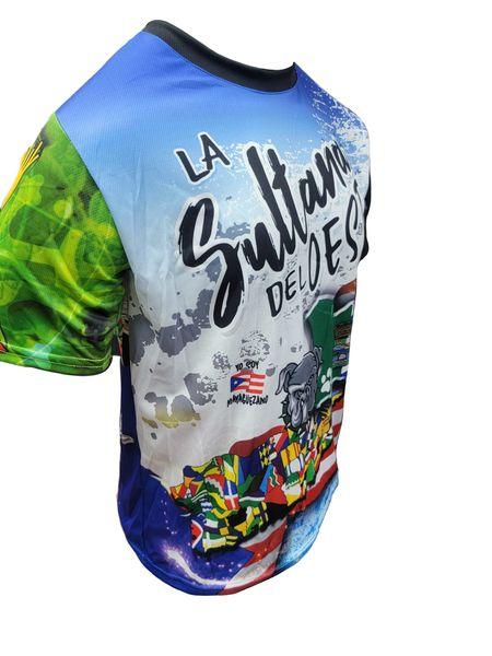 A design of a T-shirt with a front and back view. The front features "La Sultana del Oeste" in bold text, a bulldog, the Puerto Rican flag, and various international flags, with a "Gufeo" cartoon character and flag emblem. The back displays "Mayaguez" on a license plate-style graphic, a red hibiscus flower, a white star with a paw print, and the Puerto Rican flag, with a church and palm trees. The website "www.gufeo.com" is implied in the design context.